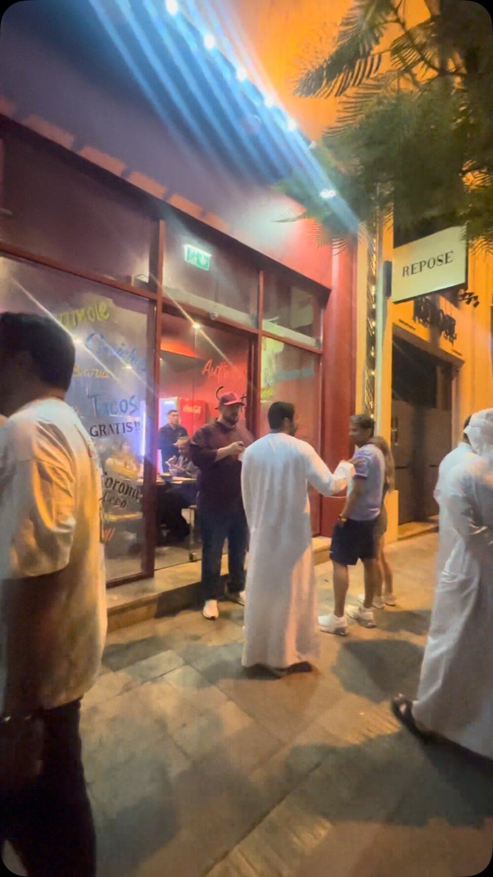 The taqueria storefront at night with guests waiting outside