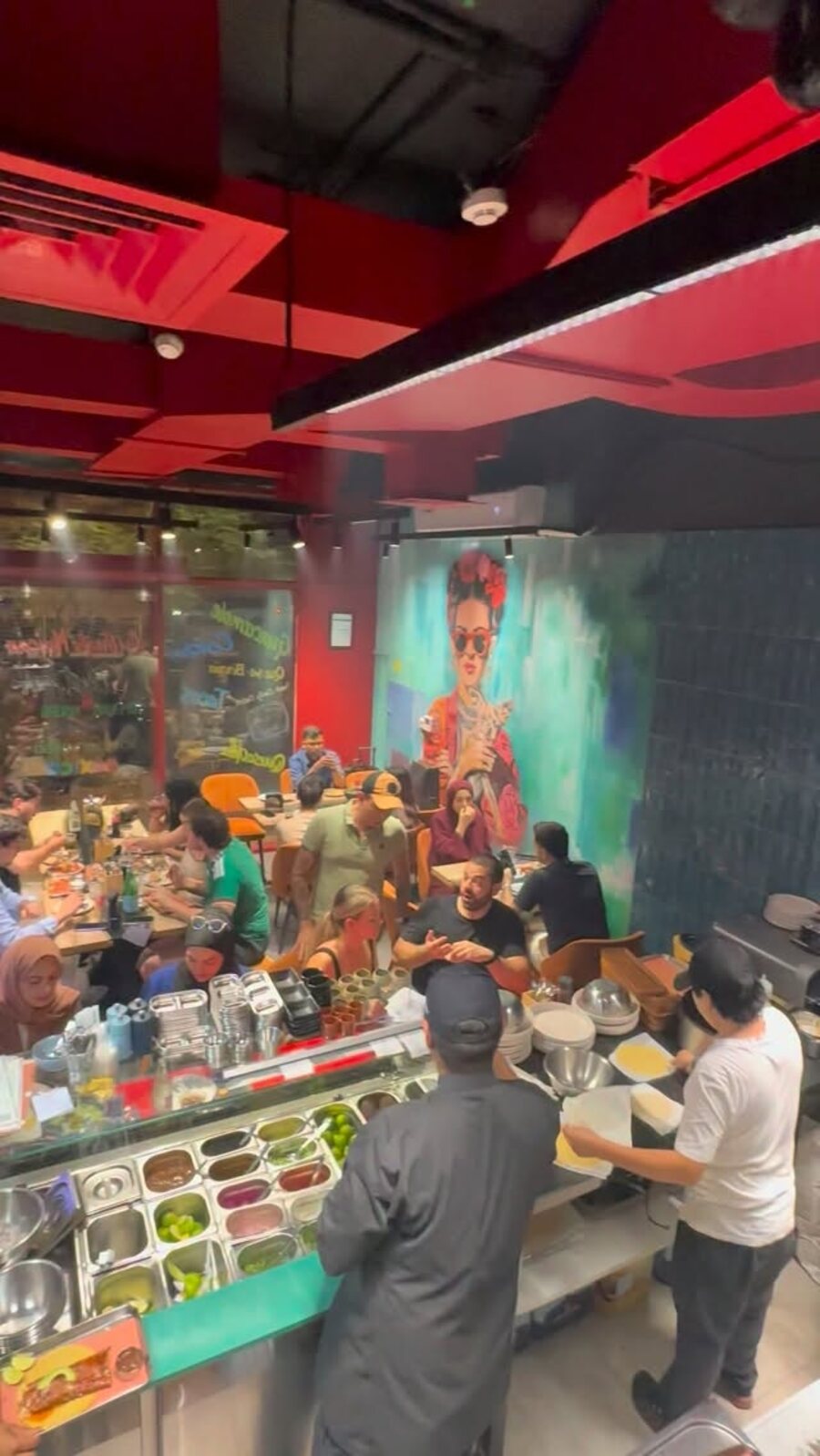 A packed dining room in front of the Frida mural and salsa bar